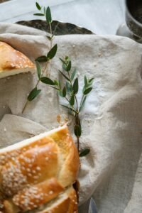 Top view of sliced challah bread with leaves on linen cloth, signifying tradition.